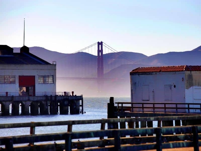 View of the San Francisco piers on a foggy day with the Golden Gate bridge appearing out of a fog, like in the San Francisco quotes you'll find on this page.