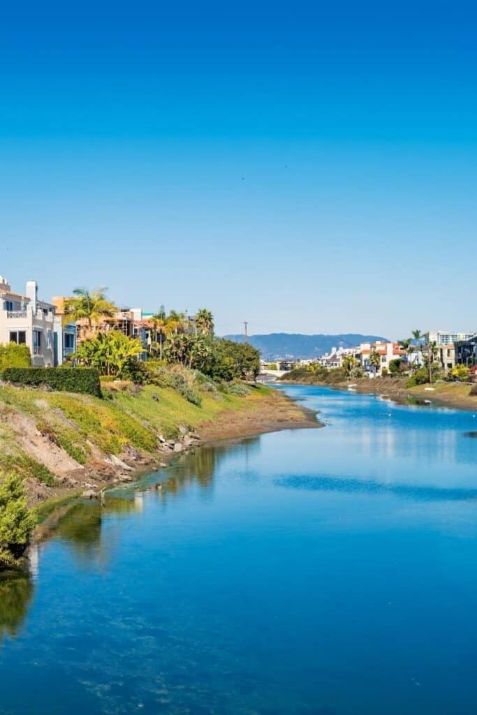 View of artificial canal with houses built one each side and hills in the distance in Venice Beach, California