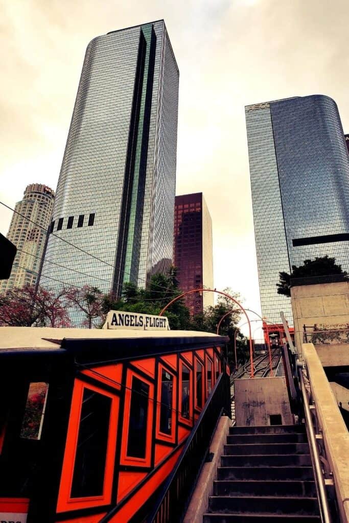 View of historic red and black "Angel's Flight" tramway with giant skyscrapers in background.