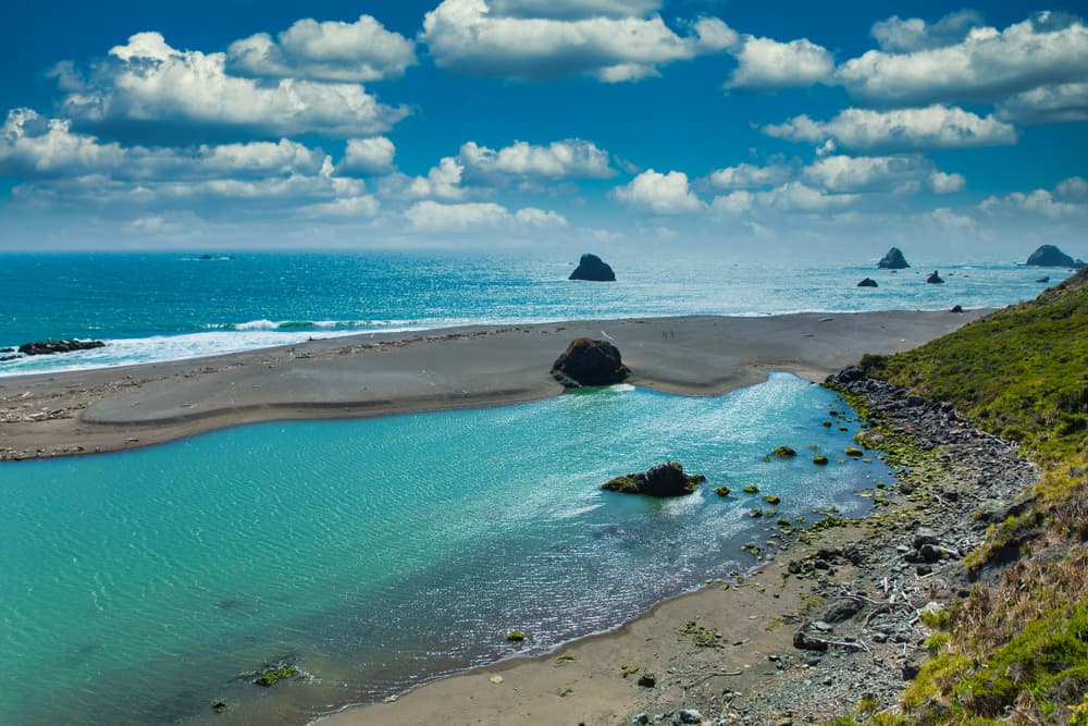 Brilliant turquoise river meeting sea with sand bar in between in Jenner