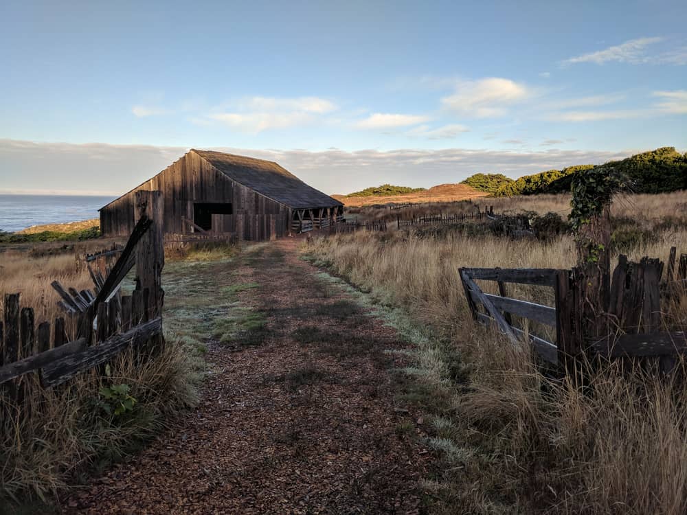 Old barn on trail with sea in background and dry grass