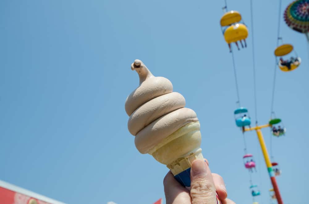 an ice cream cone held against the sky with the colorful cable cars in the sky