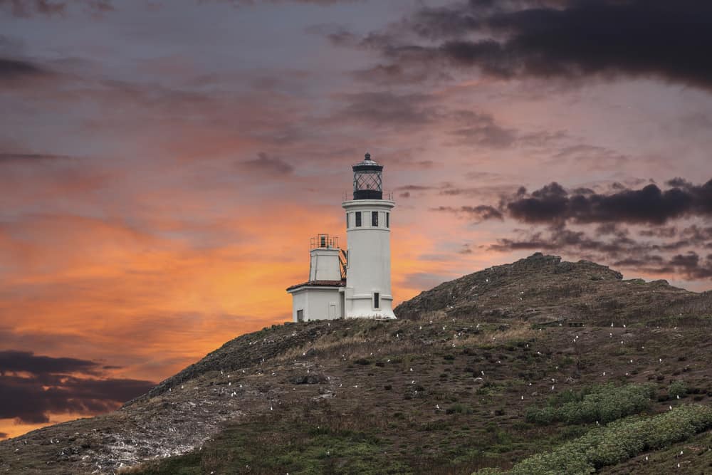 The Anacapa lighthouse, a white lighthouse on an island, seen at sunset with orange and purple colors