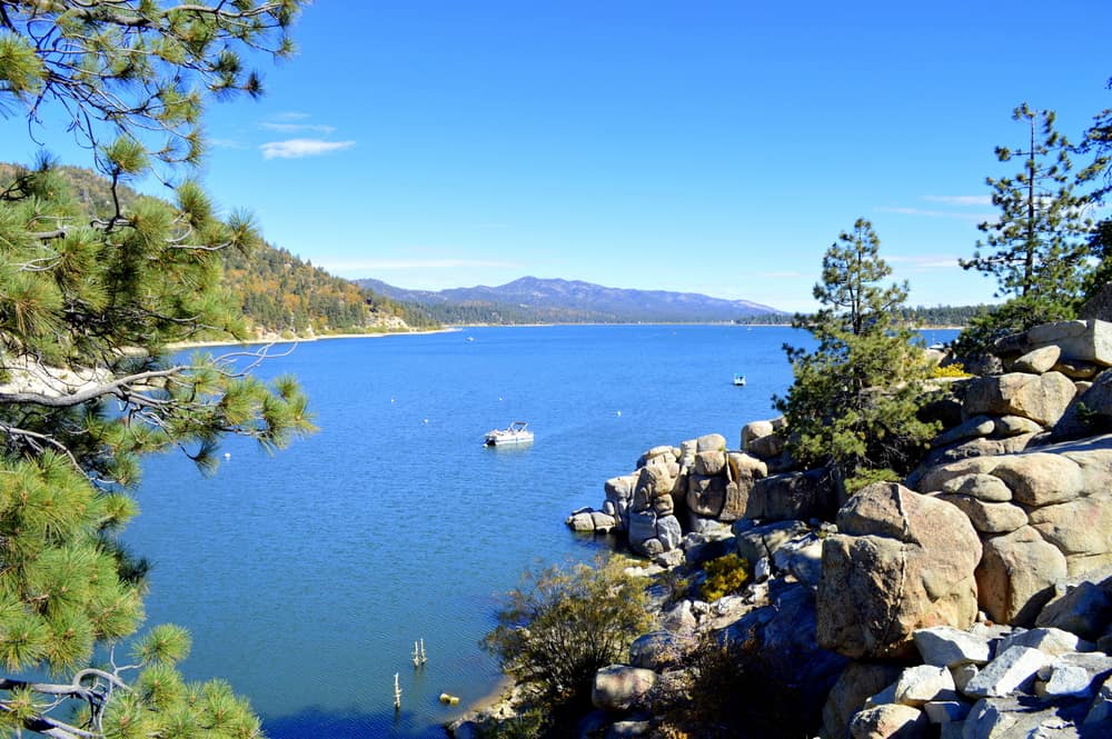 A large brilliant blue lake, surrounded by rocks and trees, with one boat out in the middle of the lake.