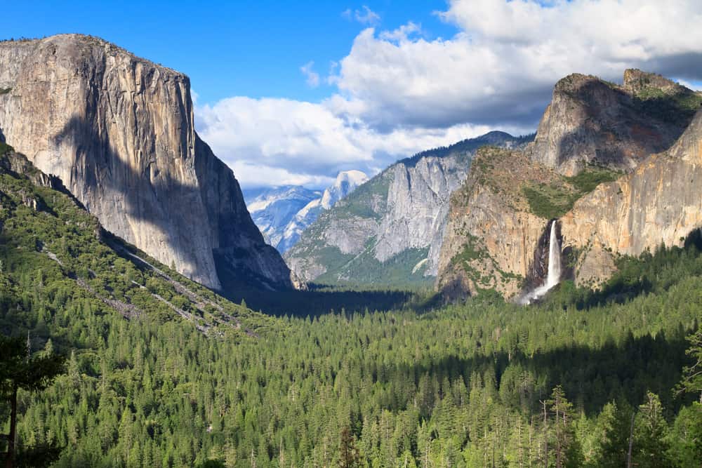 view of waterfalls, evergreen trees, granite rock faces and cloudy skies at Yosemite National Park in the early summer