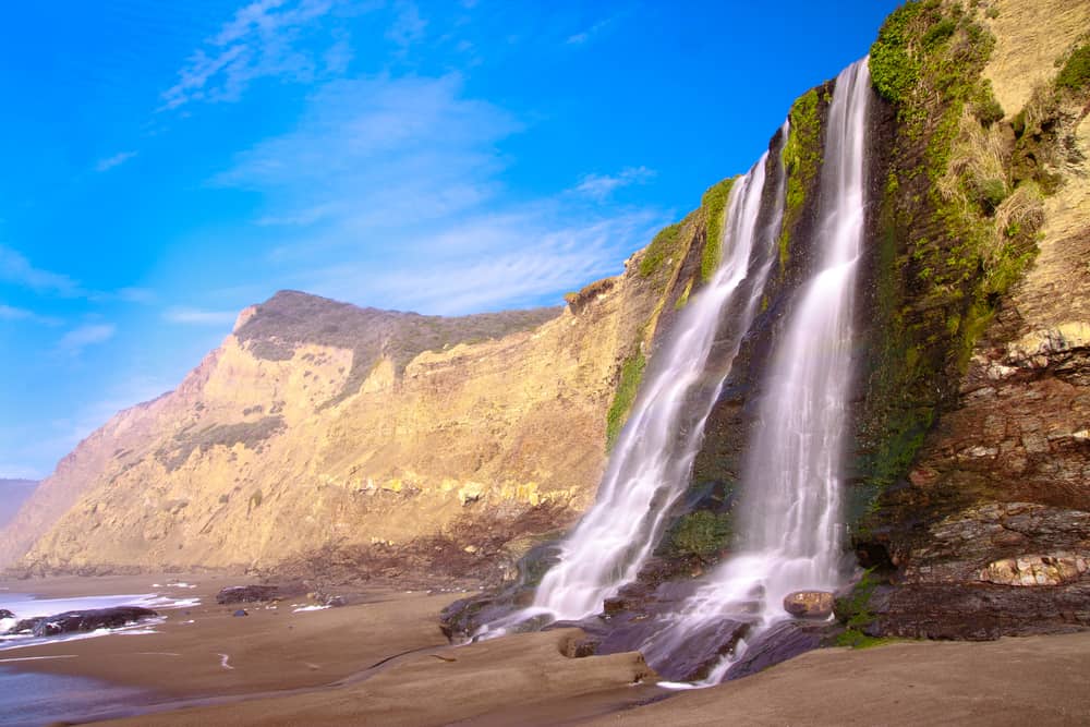 Tidefall at the endpoint Point Reyes hike, Alamere Falls, a waterfall flowing onto a beach on a sunny day.