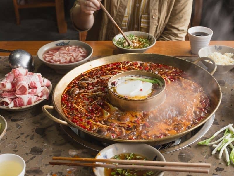 Eating Sichuan hot pot with large soup bowl raw meat and vegetables for dipping into soup and eating.