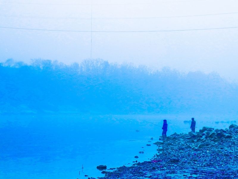 Cloudy foggy morning with two people in dark clothing fishing on side of lake