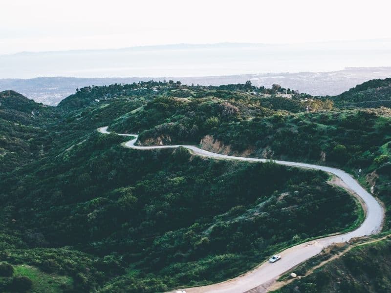 An aerial view of a mountain road in Santa Barbara with the Pacific Ocean in the background far away.