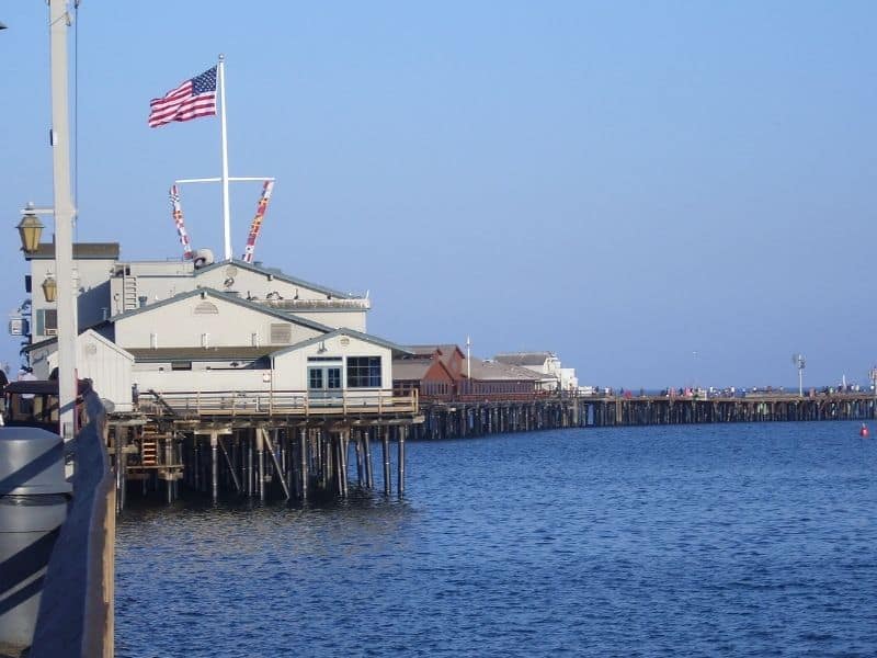 An afternoon view of the pier in Santa Barbara with old wooden structures and an American flag.