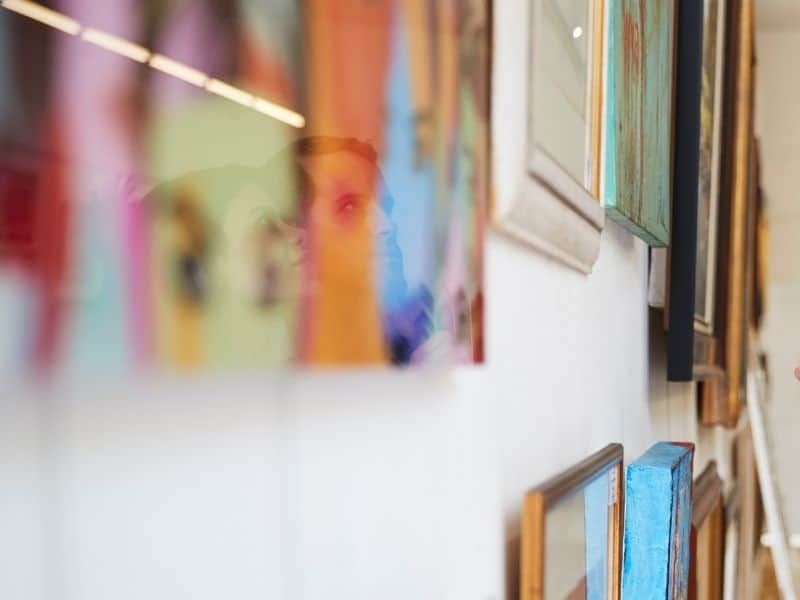 A close-up photo of gallery detail with couples face reflected in a piece of art looking at the pictures.