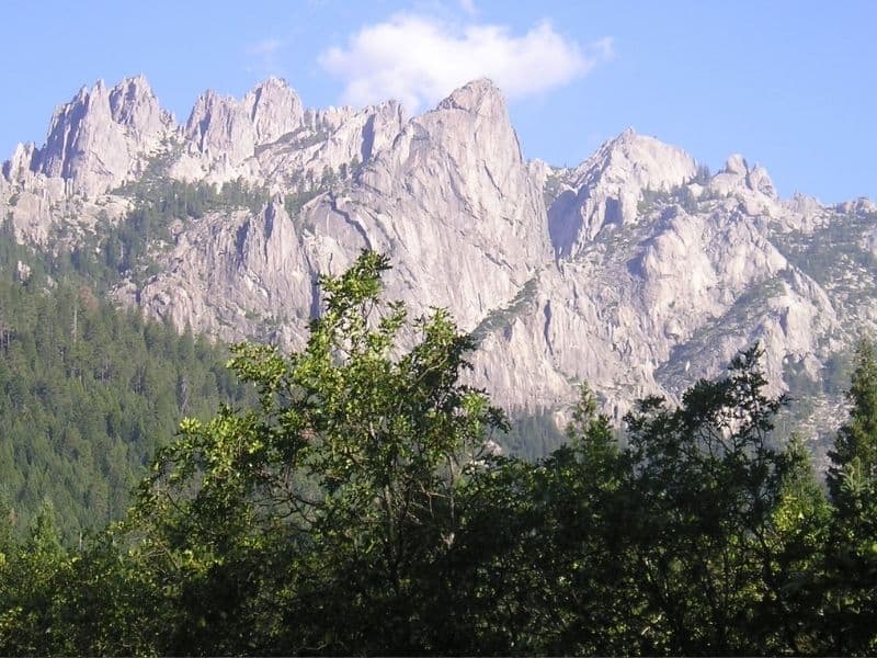 Gray craggy mountain peaks in background with some green trees and shrubbery in foreground.