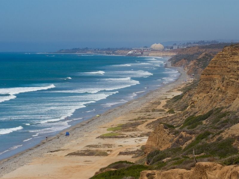 Cliffs with view of blue Pacific ocean int he background with a long sandy beach with no people