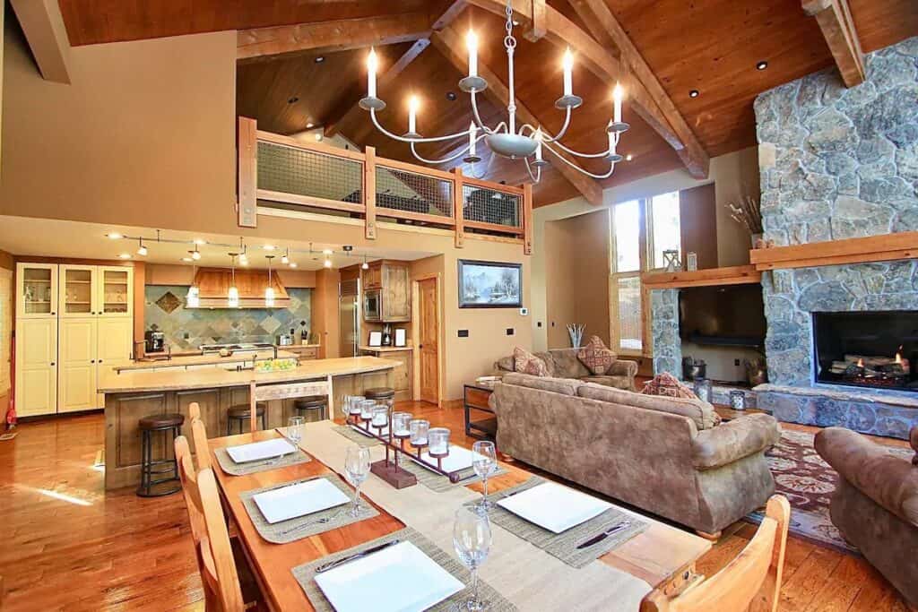 Interior photo of long dining table, fireplace with sofas, inviting cabin concept.