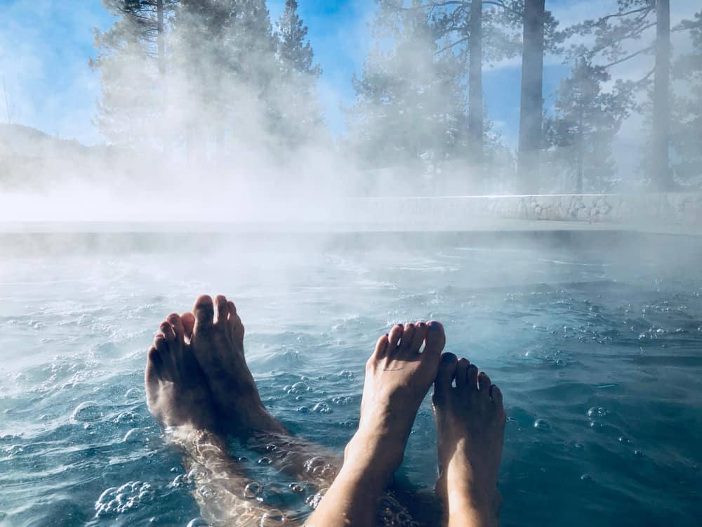 Two couples showing their feet while enjoying a hot tub pool with steam in Lake Tahoe in winter