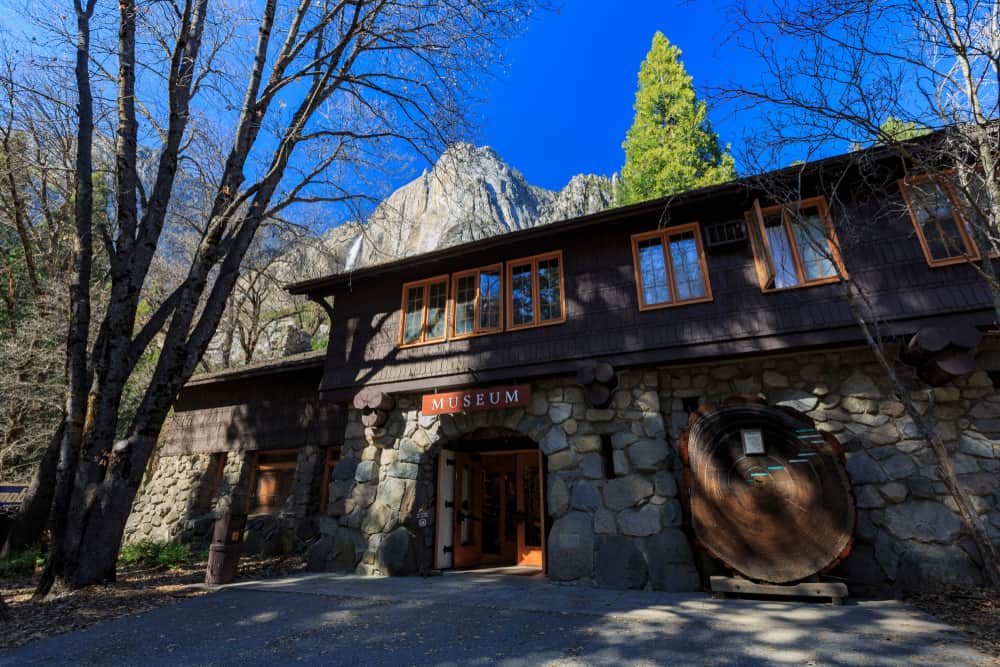 Stone building that says "museum" located in Yosemite national park with view of waterfall peeking behind the museum.