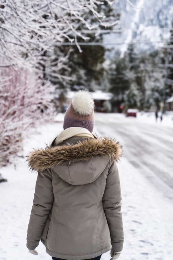 A photo of a woman wearing a pink hat and beige parka from behind on a street in Lake Tahoe in winter