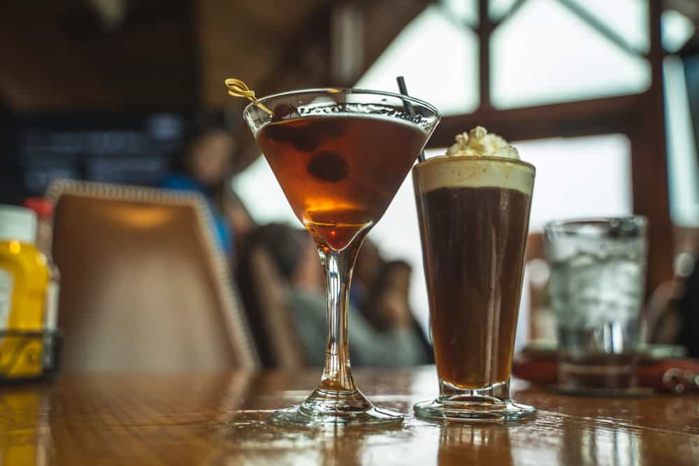 A low-angle photo of two cocktails: one is a martini with olives and the other looks to be a hot chocolate-inspired cocktail.