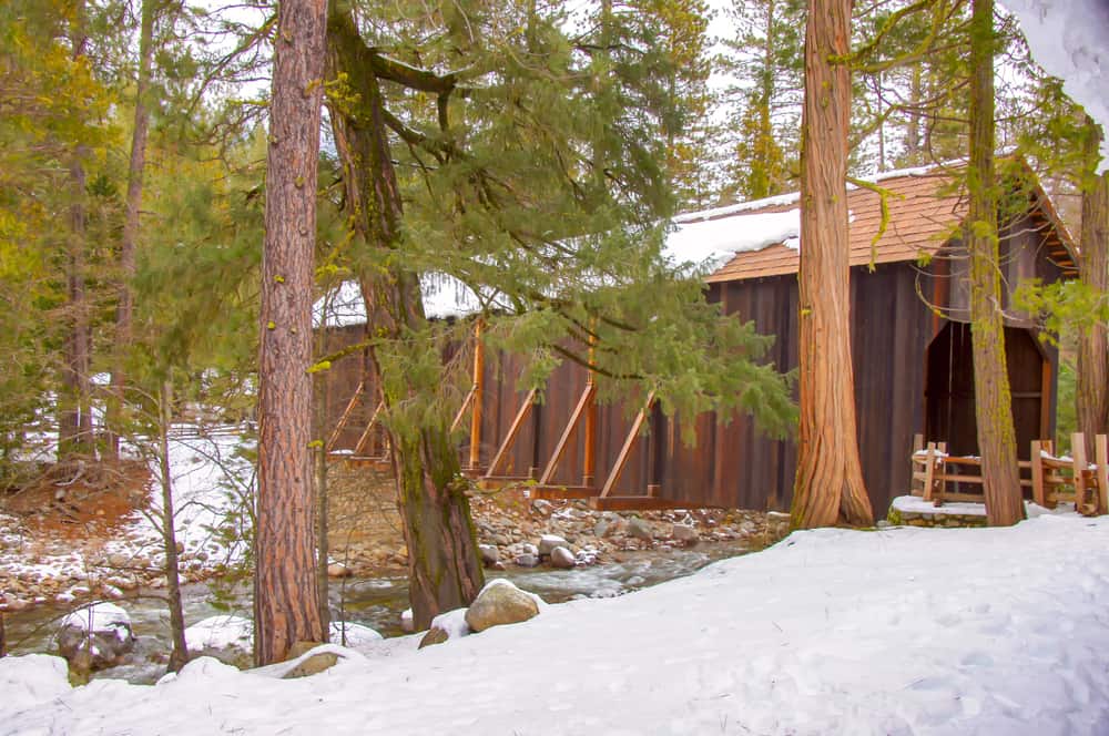 Famous Wawona covered bridge, a brown garage-like structure forming a bridge over the river with snow on top and on sides.