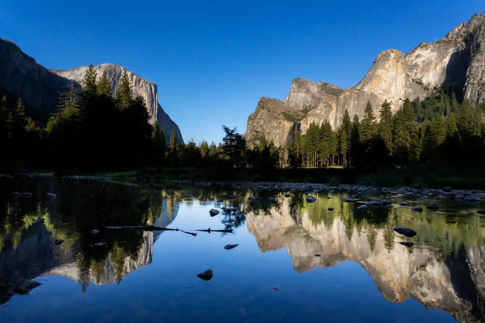 Granite cliff edges reflecting in very still water with a blue sky.