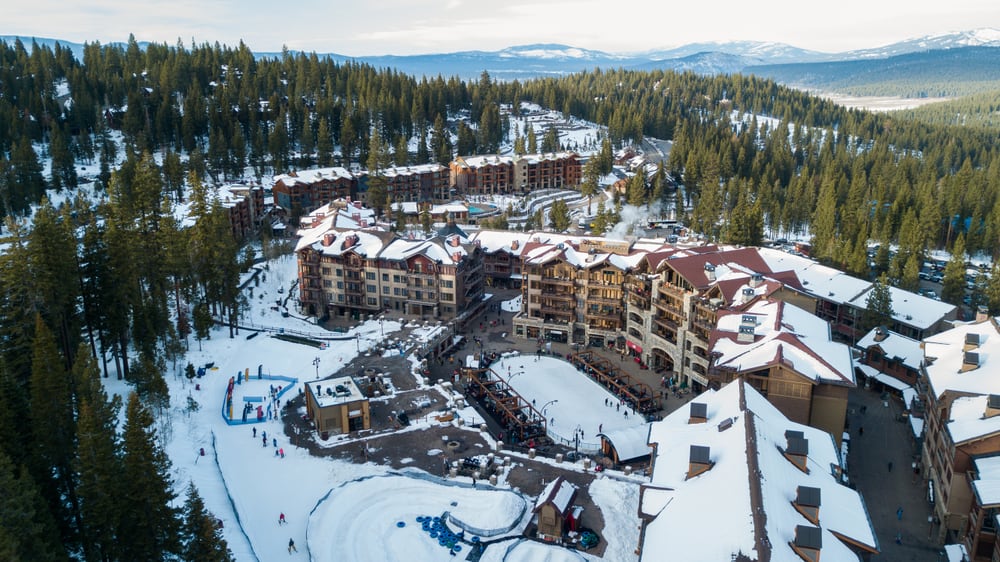 Aerial drone photo over Northstar Resort in lake Tahoe covered in snow with pine trees surrounding the facilities.