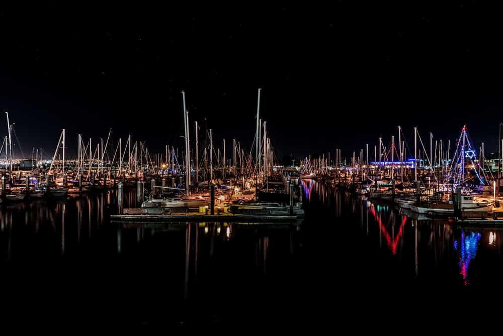 Boats and sailboats in the harbor at night with all sorts of Christmas lights reflecting in calm water.