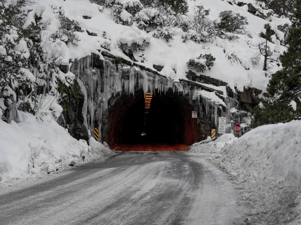 Famous Wawona tunnel with snow on sides of road with tons of snow on mountain and icicles on the opening of the tunnel.