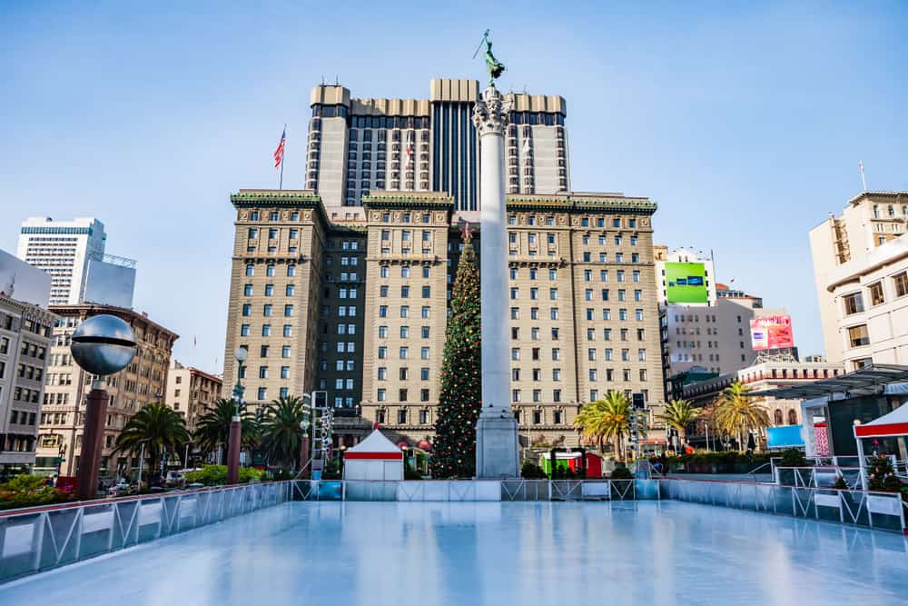 An ice rink with no one on it, with a Christmas tree and large buildings in Union Square San francisco