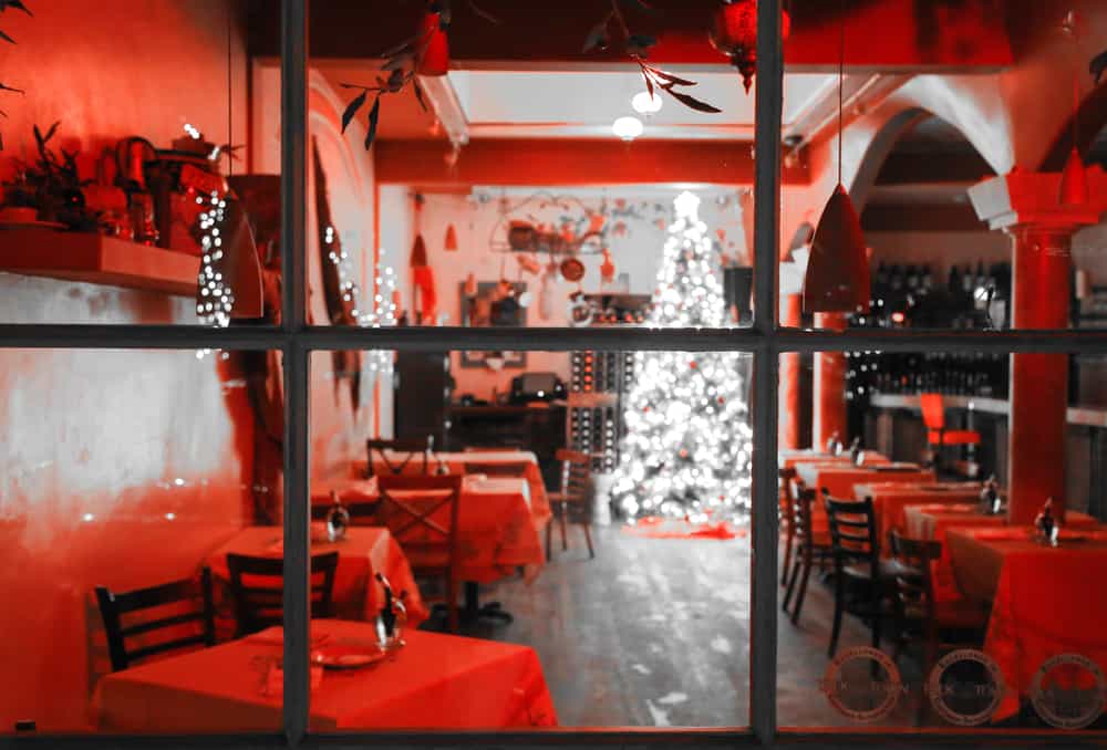 Looking through the window at a holiday-decorated restaurant in Carmel with a white lit-up Christmas tree and red interior lighting.