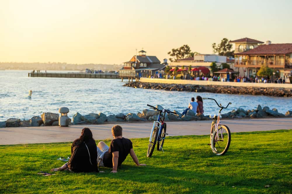 Two people with back turned to the camera with two bicycles on oceanfront boardwalk and blurry city background