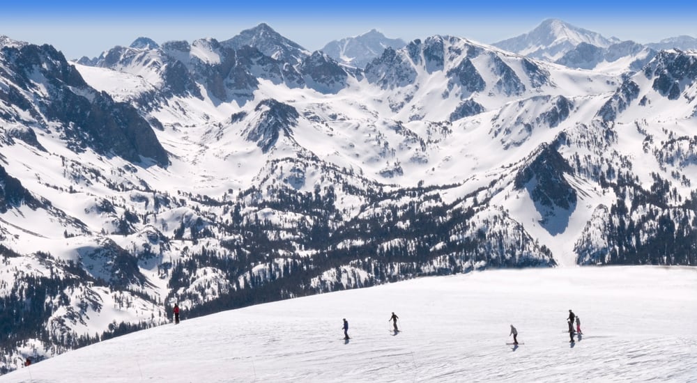 Skiers enjoying Mammoth Mountain in winter with views of Sierra Mountains in background on a sunny blue sky day.