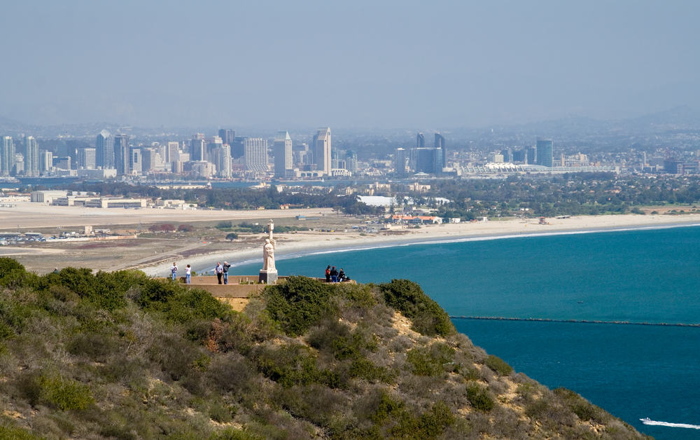 Hill with small statue with people on hill with sea and skyline of San Diego in background