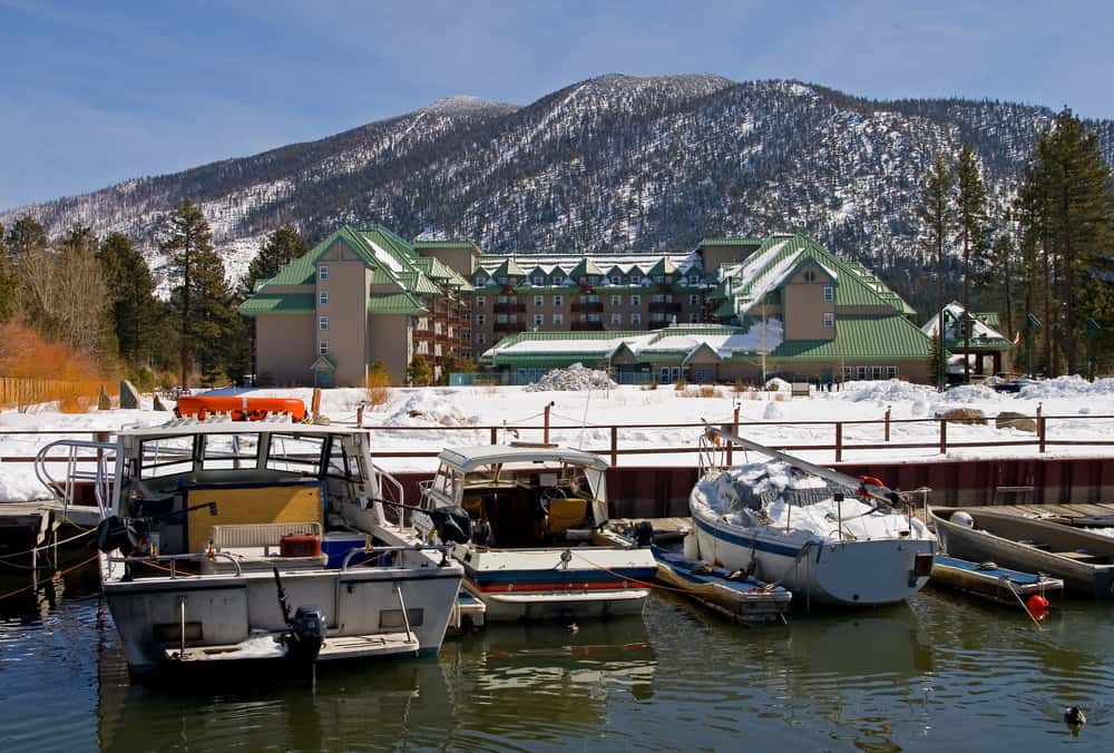 A few boats on Lake Tahoe in winter in front of a resort with a mountain in the background with snow.