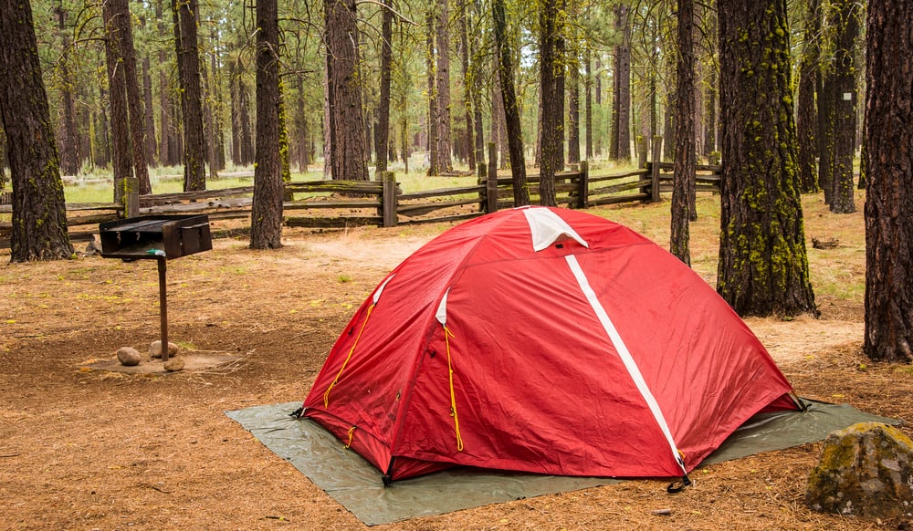 Red tent in a forest with a small unused grill next to it.