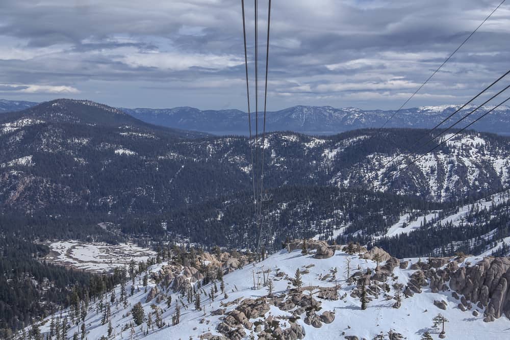 A view of the Lake Tahoe area taken from the Squaw Valley Aerial Tram with white snow, mountains, cables from the gondola, and cloudy sky.