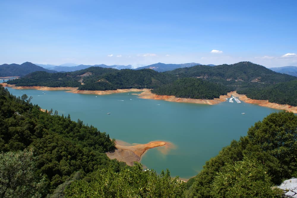 Turquoise-blue lake viewed from above angle with trees around it and boats in water.