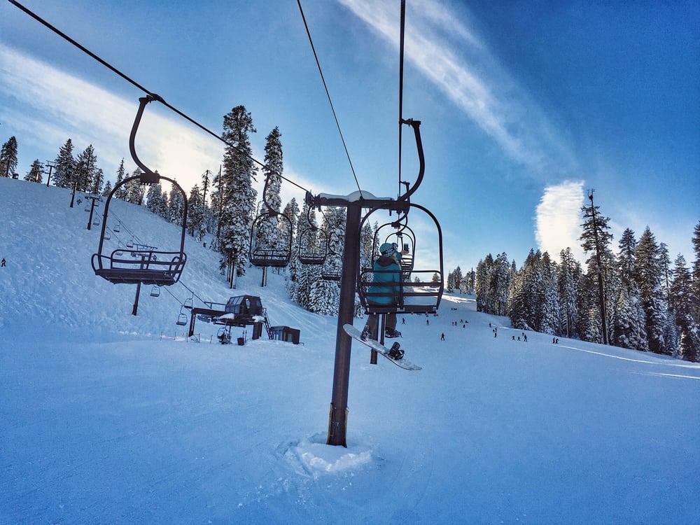 View of a woman with a snowboard solo on a chairlift in Yosemite on a bluebird winter day.