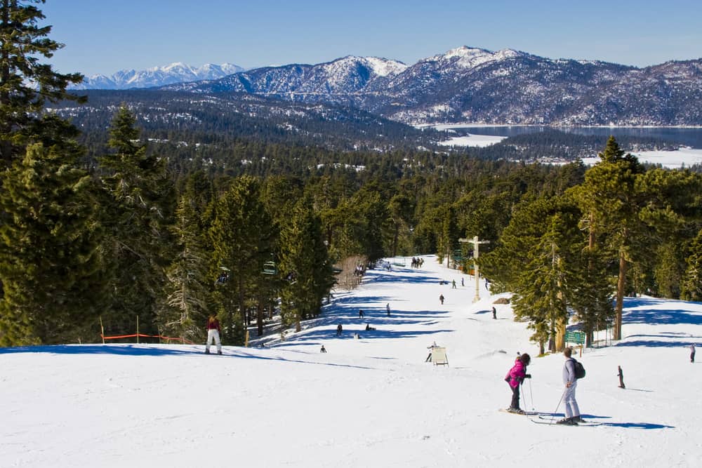 Two people talking on a downhill ski area with Big Bear Lake in background with winter scenery