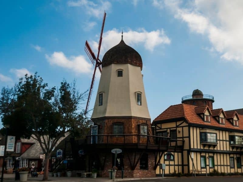 A side-angle view of Solvang's famous windmill, as well as Danish half-timber style architecture in beige and brown.