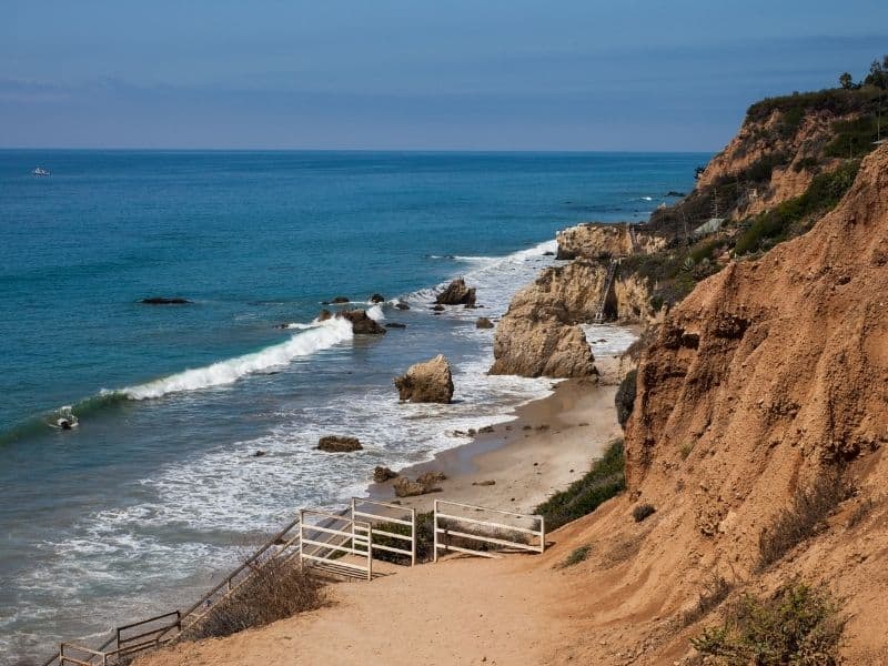 A staircase leading down to the famous El Matador beach in Malibu. Orange cliffs leading to the Pacific Ocean with a small beach with lots of rock formations.