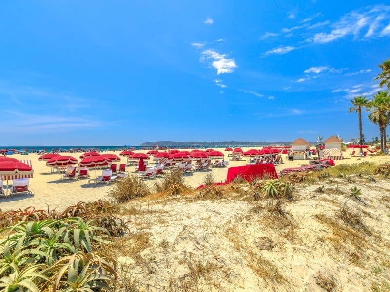 Bright red umbrellas and chairs on the fine sand of Coronado Beach in San Diego with a sunny blue sky with very few clouds.