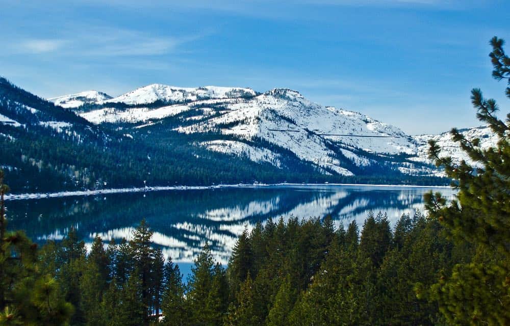 Snow-covered Donner Peak reflecting in the glassy still Donner Lake below on this popular Donner Lake hike near Tahoe.