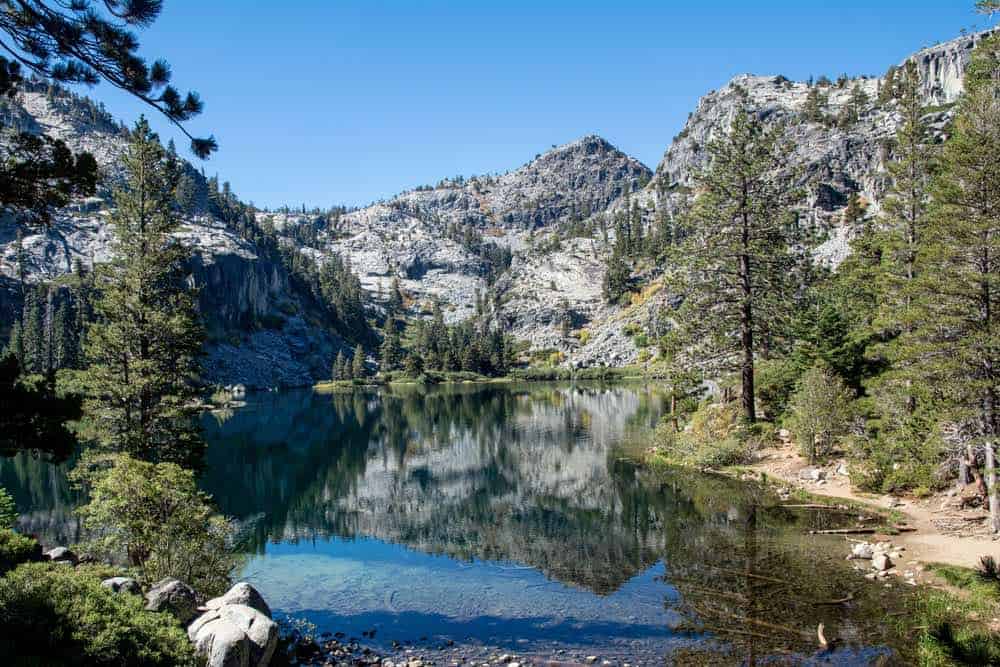 A still lake reflecting the mountain scenery back on a cloudless day, a scene from a popular hike in Lake Tahoe, from Eagle Lake.