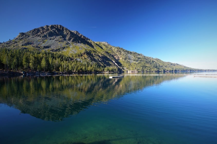 A still cerulean blue lake with a mountain reflecting in the water, seen on a clear day, on this popular day hike in Lake Tahoe