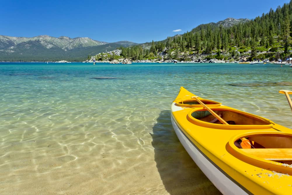 A yellow kayak contrasting with the turquoise blue waters of Lake Tahoe which are crystal clear near the beach edge