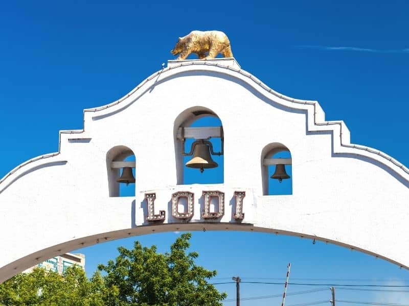 the sign for entering lodi california with a gold bear and three bells