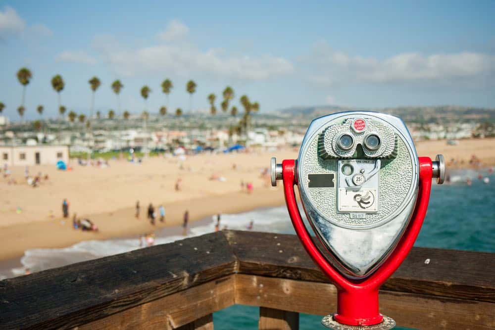 A red coin operated viewfinder looking towards the beach at Newport Beach, with palm trees fringing the shoreline.