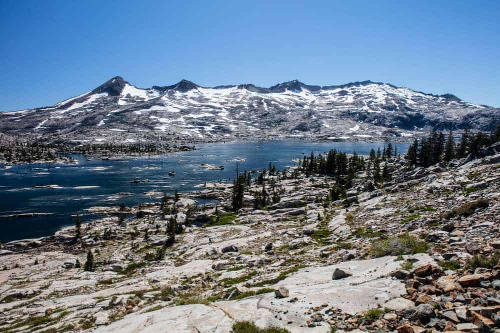 A rocky path along the Pacific Crest Trail with snowmelt forming a makeshift lake in the backcountry wilderness of California near Lake Tahoe