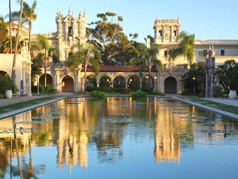 View of the pond at Balboa Park, reflecting a Spanish-colonial architecture building and lots of trees and palm trees