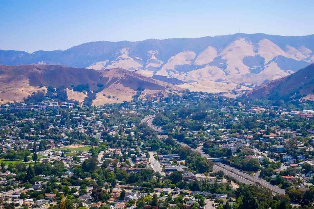 The mountainous landscape of San Luis Obispo and its tree-covered city valley floor, with yellowish grass on many of the mountains surrounding the city